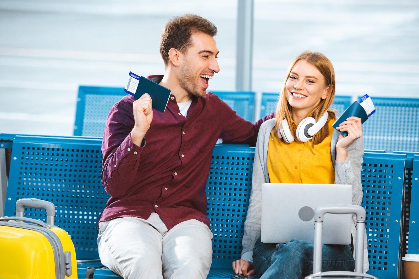 cheerful couple holding passports with air tickets in airport near luggage